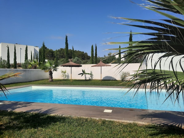 Une piscine dotée d’une terrasse carrelée, entourée de pelouse et de palmiers.