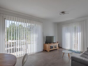Una sala de estar moderna con un televisor de pantalla plana sobre un mueble de madera, un sofá gris y una mesa de comedor con sillas.
