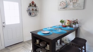 A dining area with a table set for four, a shelf with decorative items, and a painting on the wall. - Bungalow at the Bayou close to downtown and bases (Pensacola)