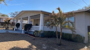 A single-story house with a covered porch, a small garden with palm trees, and a clear blue sky. - Bungalow at the Bayou close to downtown and bases (Pensacola)