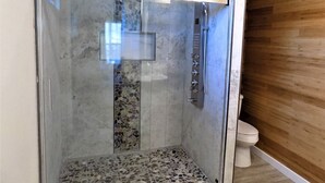 A glass-enclosed shower with a tiled floor, a wall-mounted faucet, and a wooden panel wall adjacent to a toilet. - Bungalow at the Bayou close to downtown and bases (Pensacola)