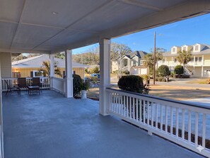 A covered porch with a railing, outdoor seating, and a view of a residential area.