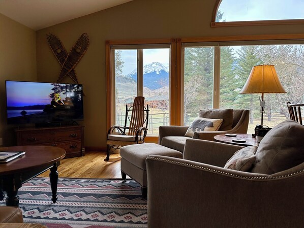 A living room with a large window, a television, a sofa, a chair, and a lamp. - RIVERSIDE LODGE: wildlife watching, fishing, hiking from the house. Next to YNP! (Gardiner)