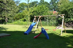 Une aire de jeux avec un toboggan, une balançoire et une petite structure en bois.