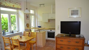 A kitchen with a dining table and chairs, a television on a dresser, and a window with curtains. - Idyllic apartment 10 minutes to the beach (Barkelsby)