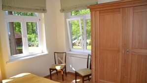A bedroom with a bed, two chairs, a wooden wardrobe, and a window with a view of greenery. - Idyllic apartment 10 minutes to the beach (Barkelsby)