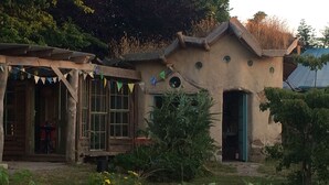 A rustic building with a wooden porch and a green door, surrounded by a garden with yellow flowers. - Eco Glamping immersed in nature, ideal for family holidays andromantic getaways! (Whitegate)
