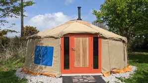 A small, single-room yurt with a wooden door and a blue window, surrounded by gravel and grass. - Eco Glamping immersed in nature, ideal for family holidays andromantic getaways! (Whitegate)