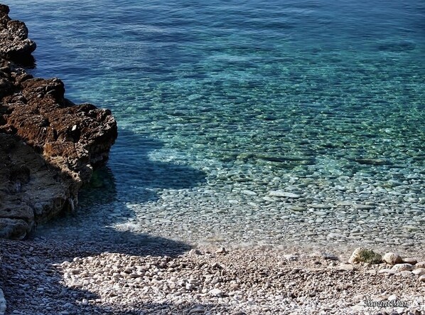 A rocky shoreline with clear water and pebbles.