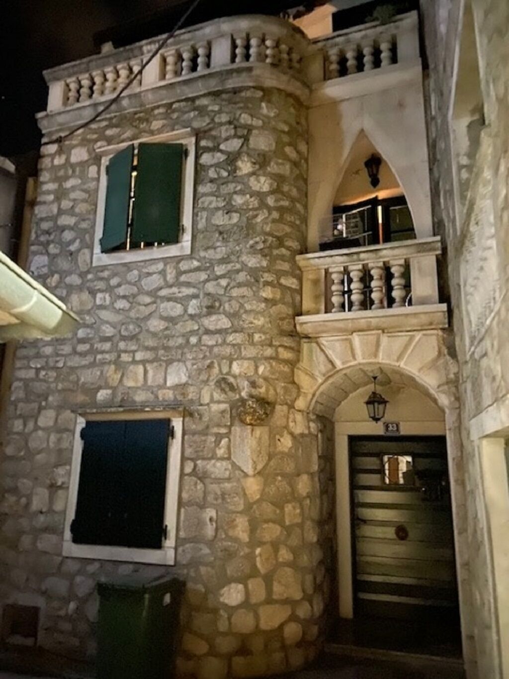 Un bâtiment en pierre doté d’un balcon, d’une porte avec un numéro et d’une poubelle.