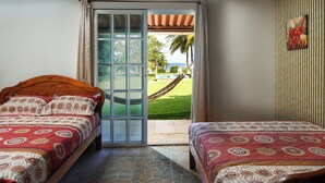 A bedroom with two beds, a view of a garden, and a hammock outside.