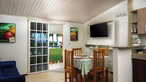 A dining area with a table set for four, wooden chairs, a television mounted above the counter, and a coffee machine.