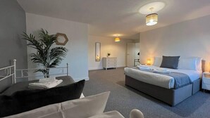 A modern hotel room with a large bed, a desk, and a chair. There is a plant and a mirror on the wall. - Shrewsbury Townhouse with Open Plan Living (Shrewsbury)