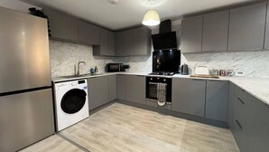 A modern kitchen with grey cabinets, a stainless steel refrigerator, a washing machine, a microwave, a stove, and a hanging light fixture. - Shrewsbury Townhouse with Open Plan Living (Shrewsbury)