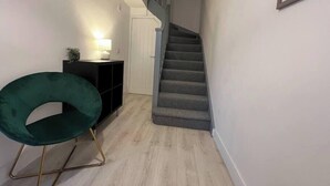 A narrow hallway with a green chair, a small table with a lamp, and a staircase. - Shrewsbury Townhouse with Open Plan Living (Shrewsbury)
