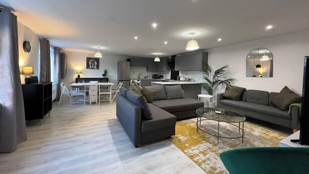 A modern living room with a grey sofa, a glass coffee table, and a dining area with a white table and chairs. - Shrewsbury Townhouse with Open Plan Living (Shrewsbury)