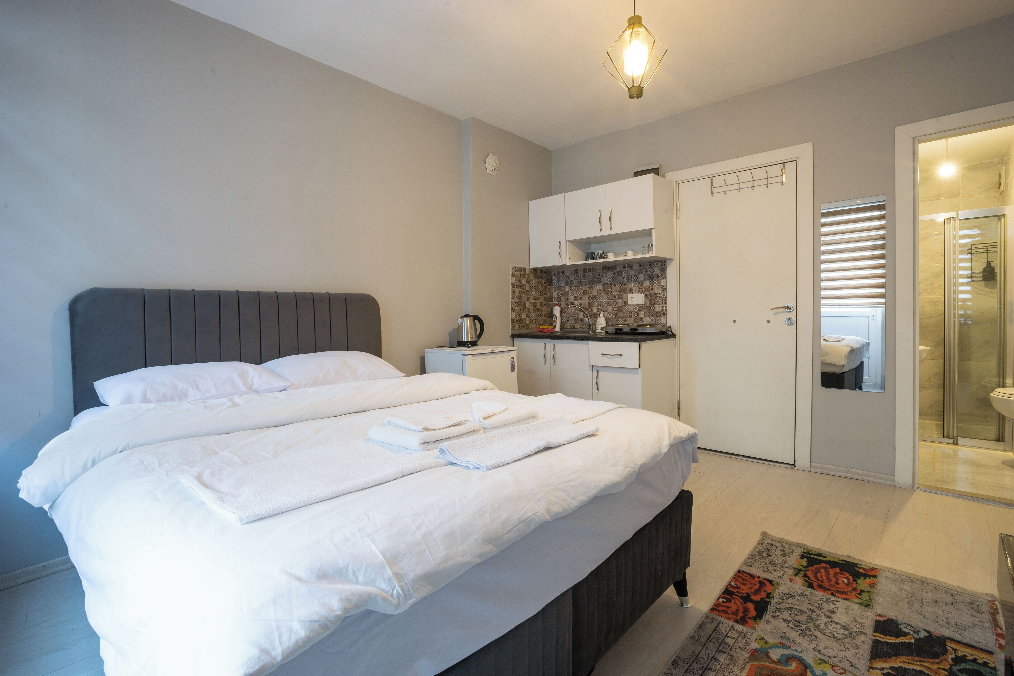 Une chambre dotée d’un grand lit, d’une table de chevet avec une bouilloire, d’un petit coin cuisine et d’une salle de bain avec une douche en verre.