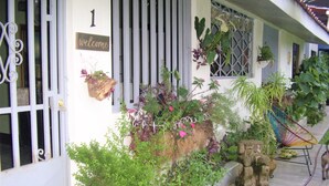 A house with a white exterior, a 'welcome' sign, a metal gate, and various potted plants.