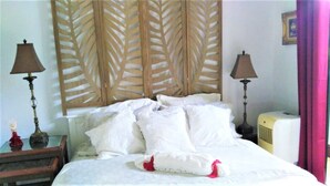 A hotel room with a bed, two bedside lamps, a decorative headboard, a bedside table with a lamp, and an air conditioner.