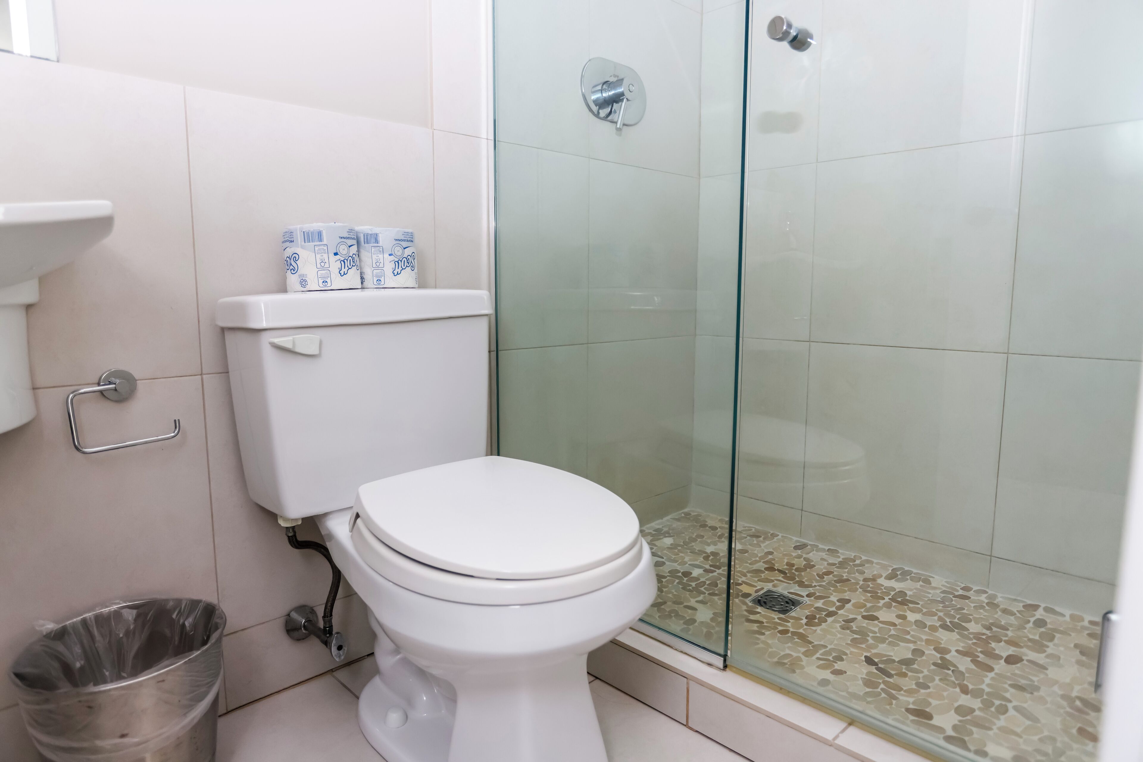 A bathroom with a toilet, a glass shower enclosure, and a trash bin.