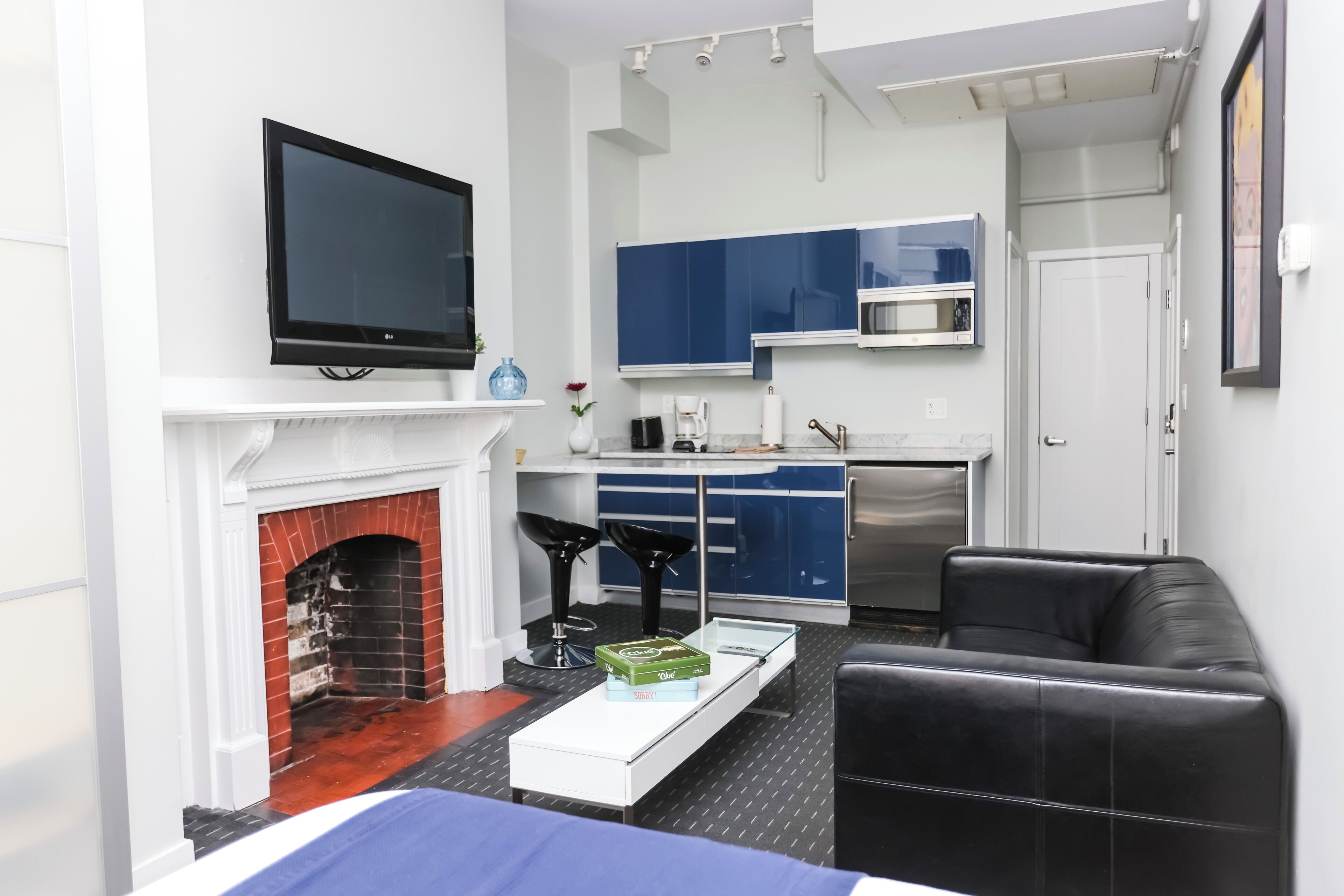 Ein modernes Wohnzimmer mit Kamin, Flachbildfernseher, einem schwarzen Ledersofa und einer Küchenzeile mit blauen Schränken und einer Mikrowelle.