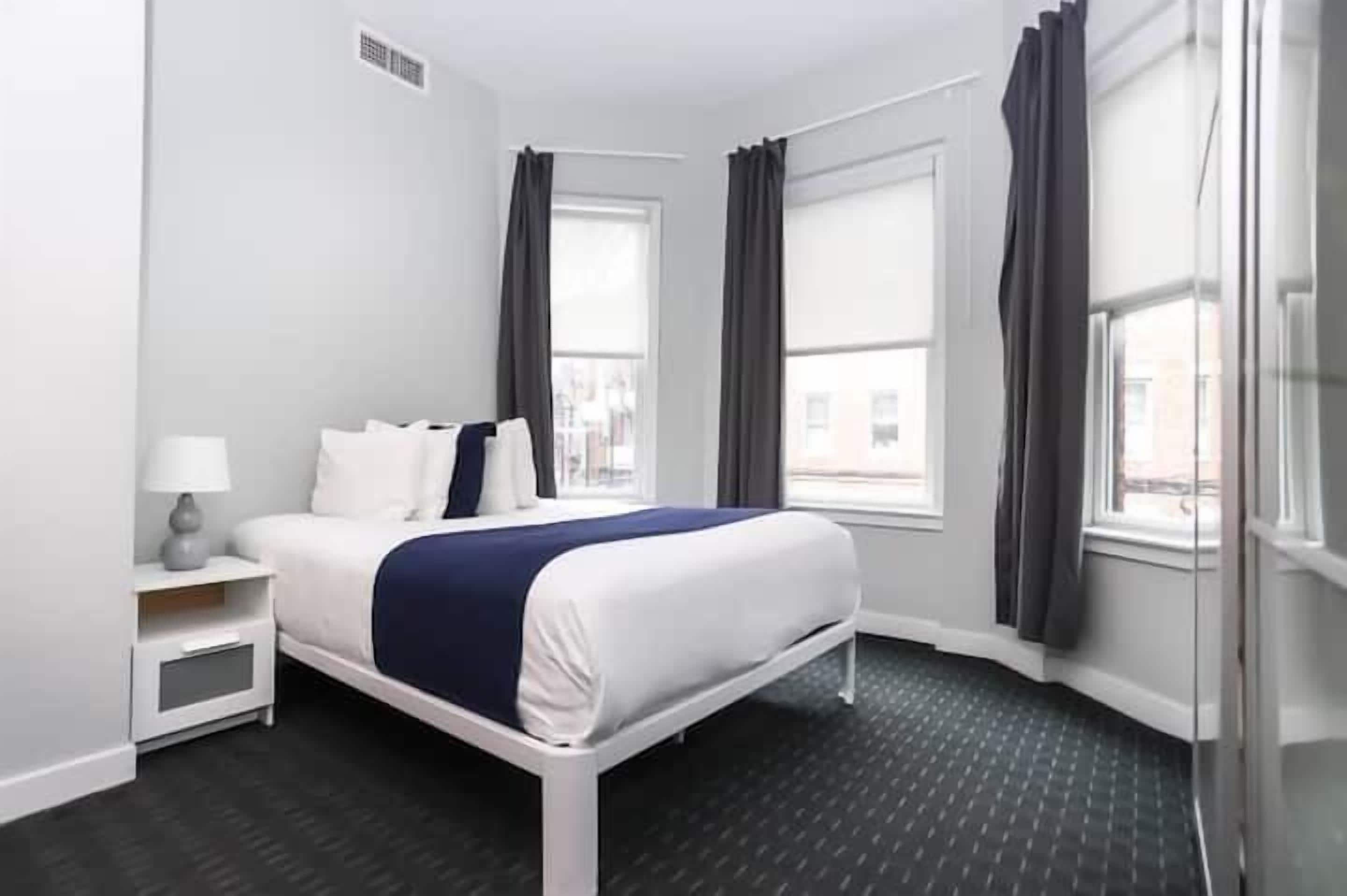 A hotel room with a bed, a nightstand, a window, and a view of the outside.