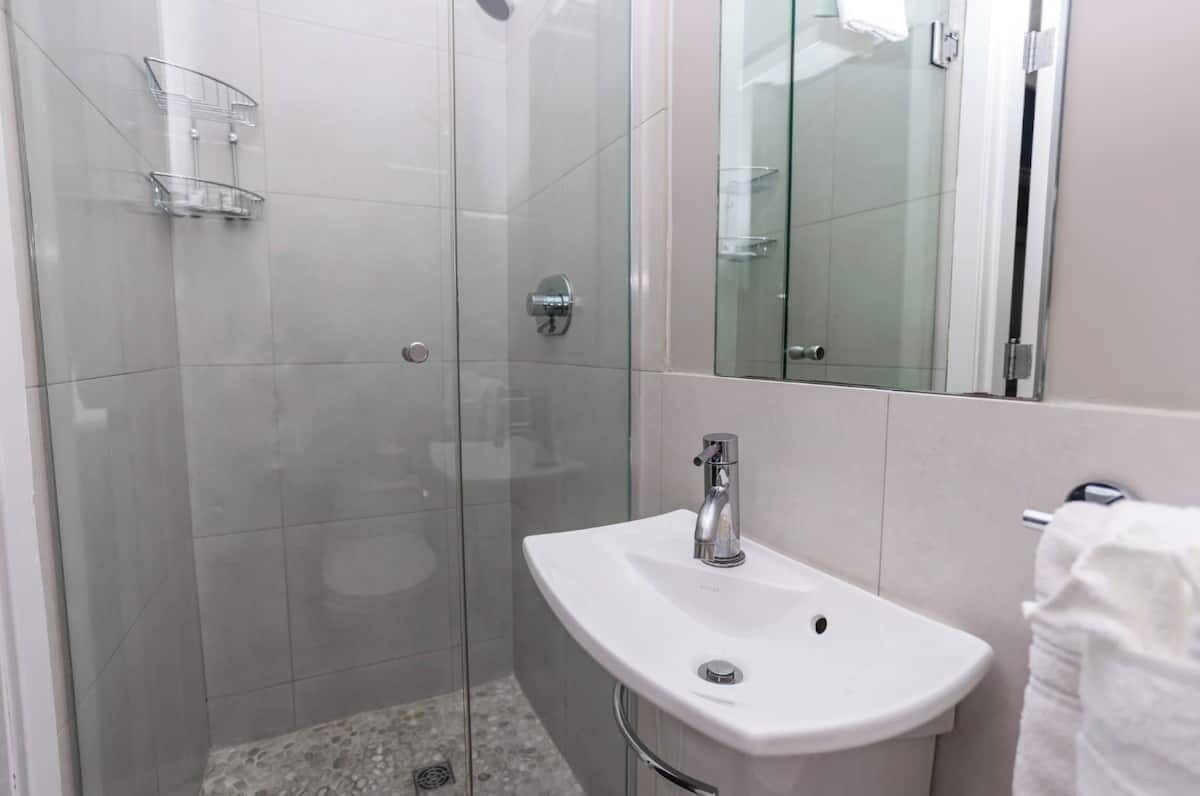 Uma casa de banho moderna com cabine de duche em vidro, lavatório branco e espelho.