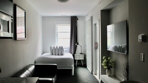 A hotel room with a bed, a desk, a chair, a TV, a mirror, a window with curtains, and a vase with flowers.