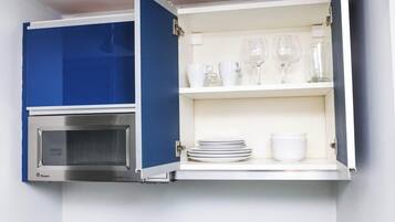Cocina con microondas incorporado y un armario con estantes que contienen vajilla y vasos blancos.