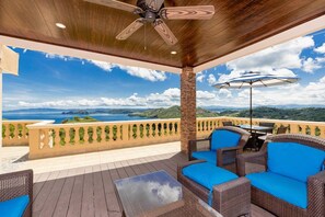 A covered outdoor seating area with wicker furniture and a table, overlooking a scenic landscape. - Bella Vista – Casa Q • 2 BR Penthouse Retreat • Rooftop Terrace & Ocean Views • 5 Guests (Playa Hermosa)