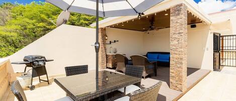 An outdoor patio with a dining table, chairs, a grill, and a ceiling fan.