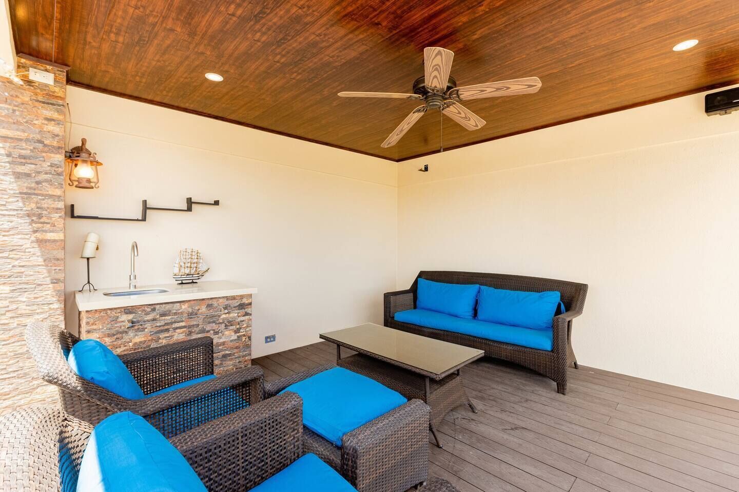 Un espace extérieur aménagé en terrasse, avec des meubles en osier, un bar intégré et un ventilateur de plafond.