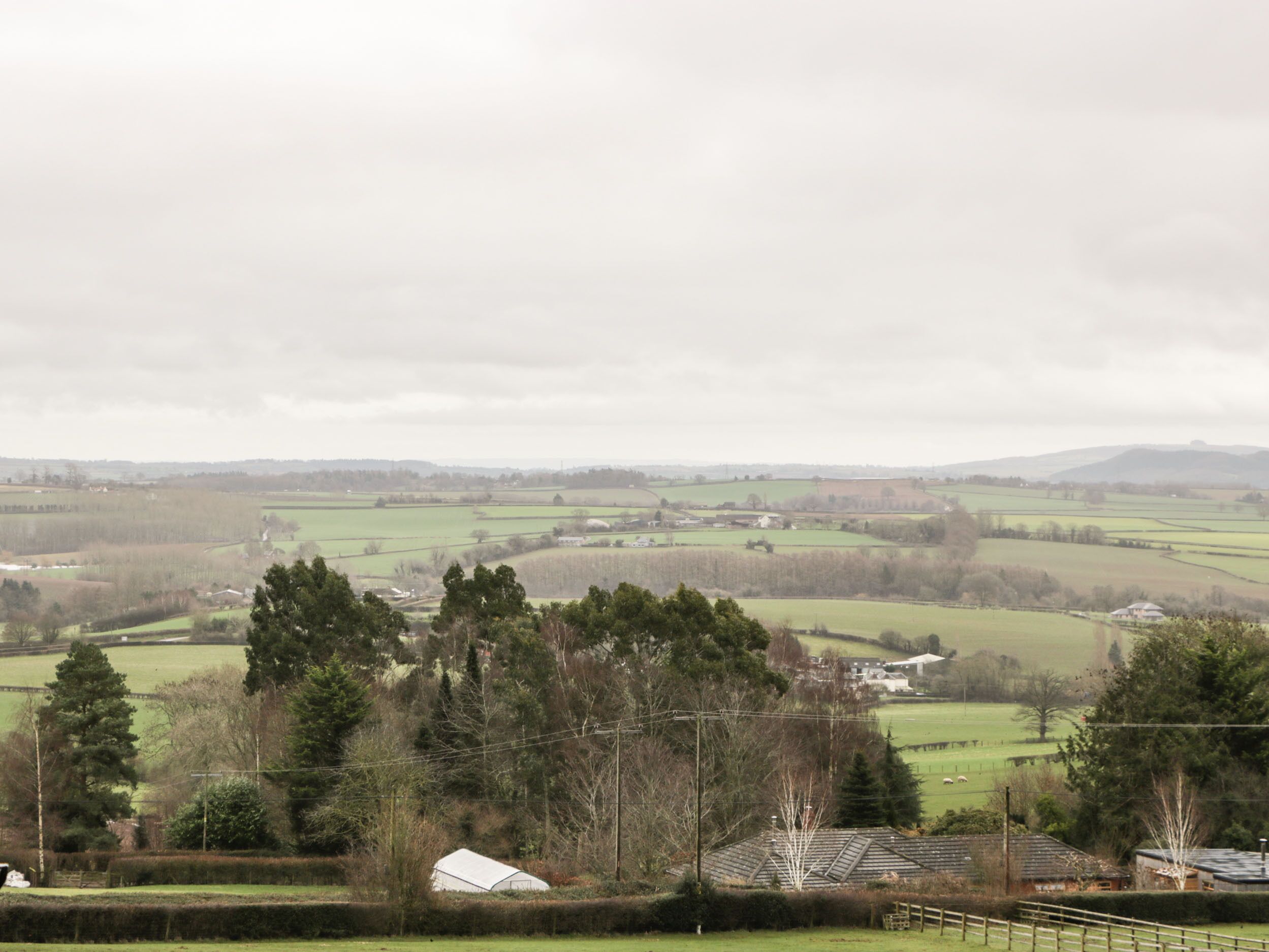 A rural landscape with fields, trees, and a few buildings.