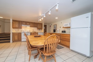 A kitchen with wooden cabinets, a white refrigerator, a dining table with chairs, and a microwave.