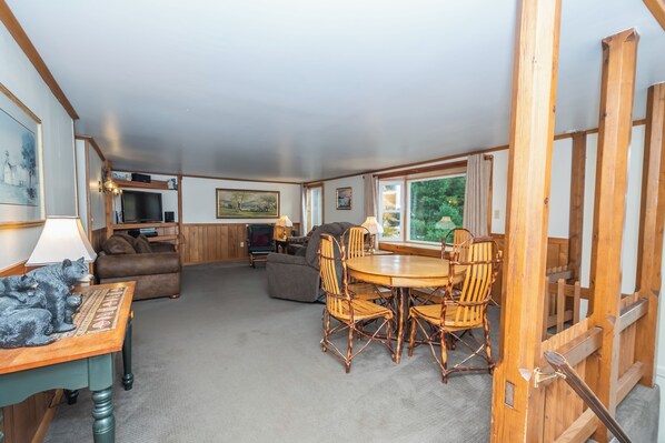 A cozy living room with a wooden dining table, comfortable seating, and a television in the background.
