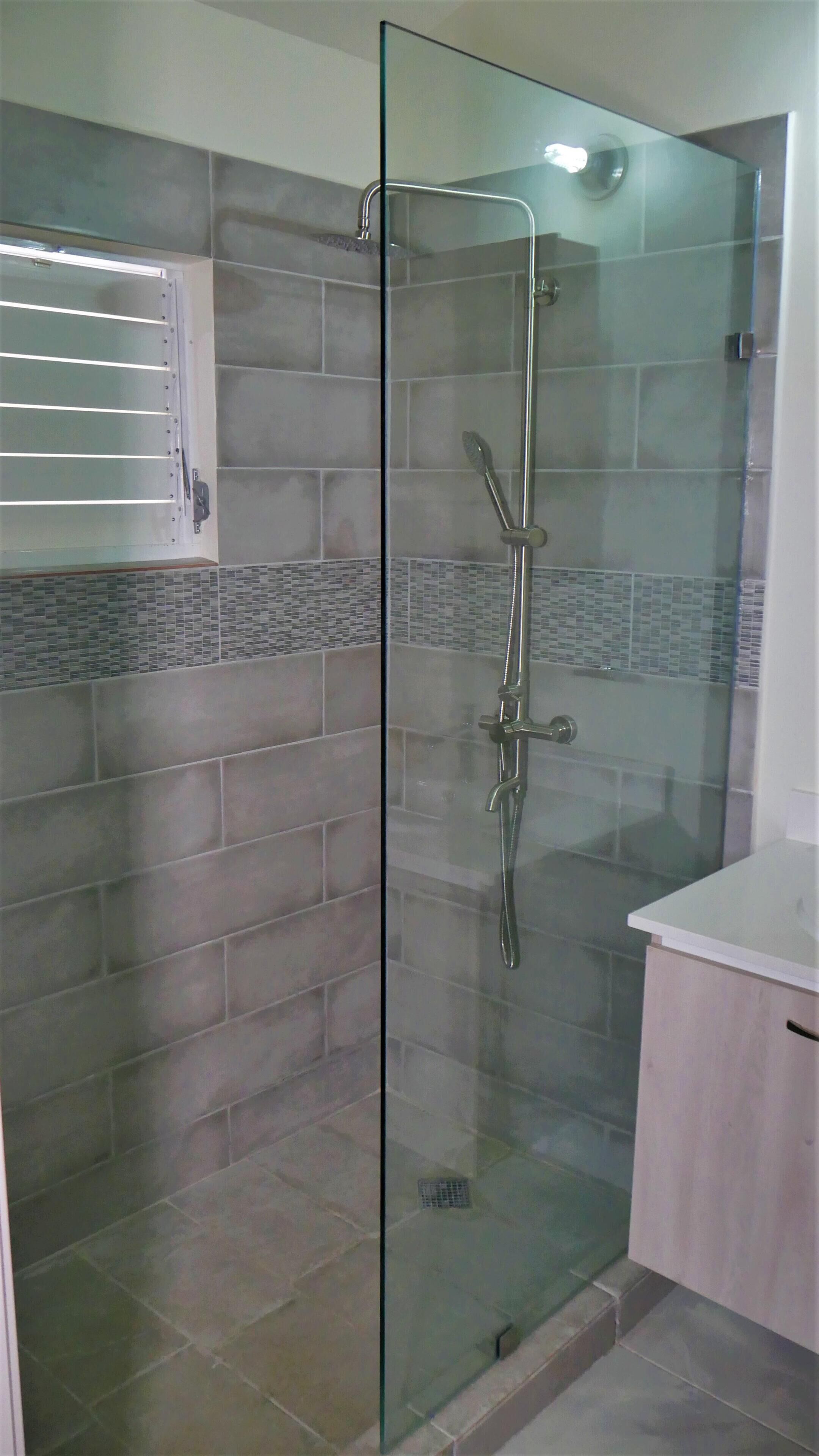 A glass-enclosed shower with a tiled wall and a white countertop to the right.