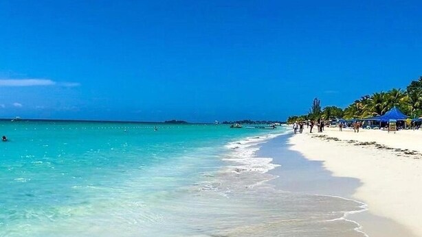 A beach with clear turquoise water, a sandy shore, and a few people walking. - Lux Sea View Camelot Village Discovery Bay (Discovery Bay)
