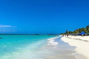 A beach with clear turquoise water, a sandy shore, and a few people walking. - Lux Sea View Camelot Village Discovery Bay (Discovery Bay)
