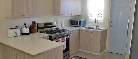 A compact kitchen with a gas stove, microwave, toaster, and a sink.