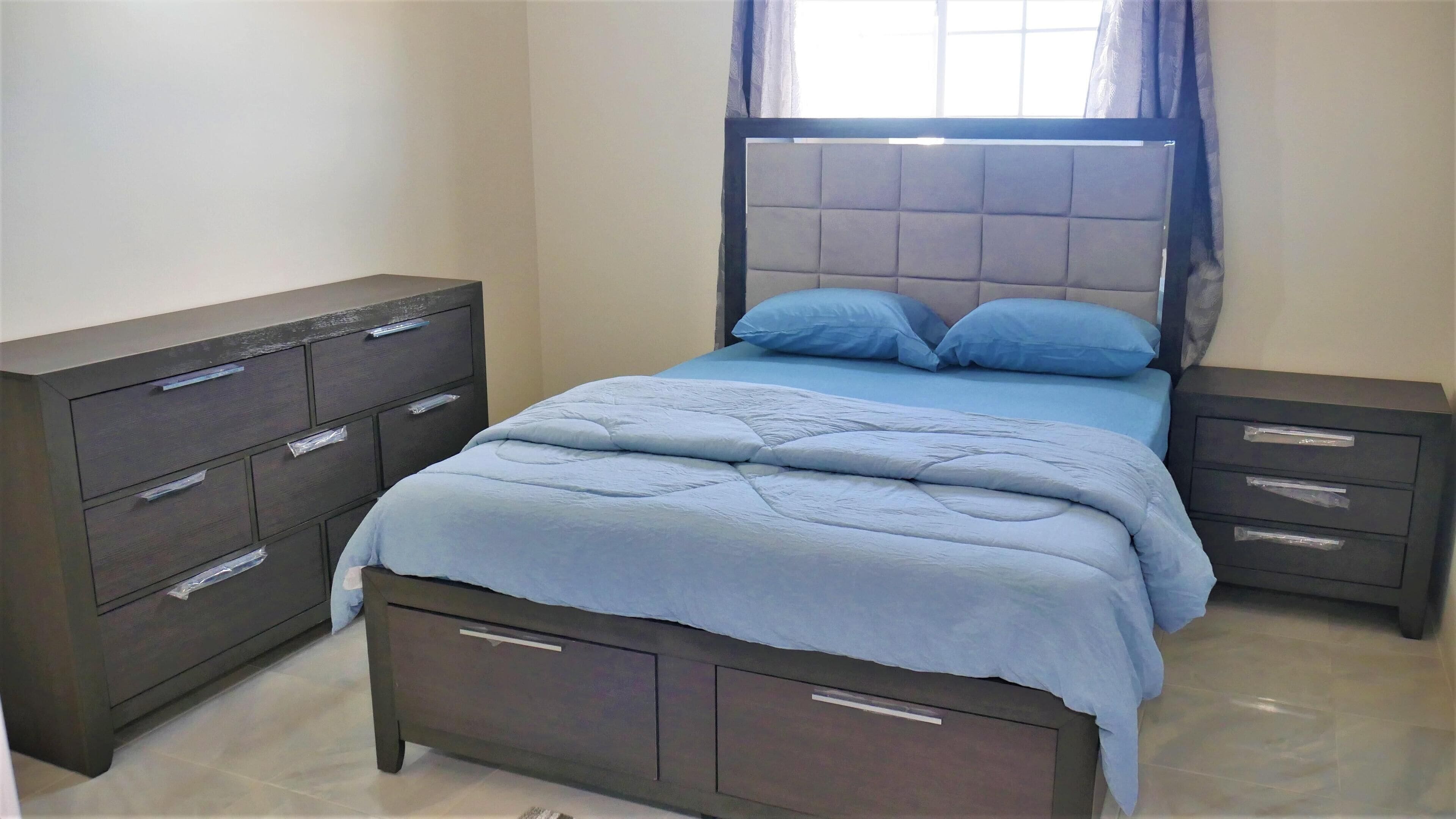 Un dormitorio con cama, dos mesitas de noche, cómoda y ventana con cortinas.