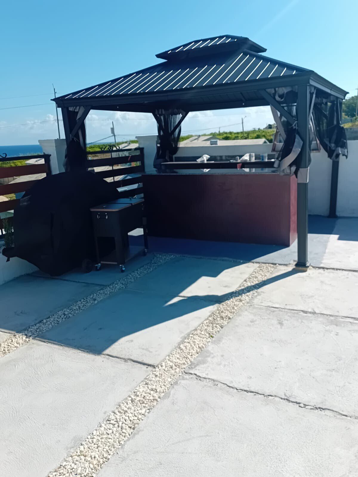 A covered outdoor seating area with a grill, benches, and a view of the ocean.