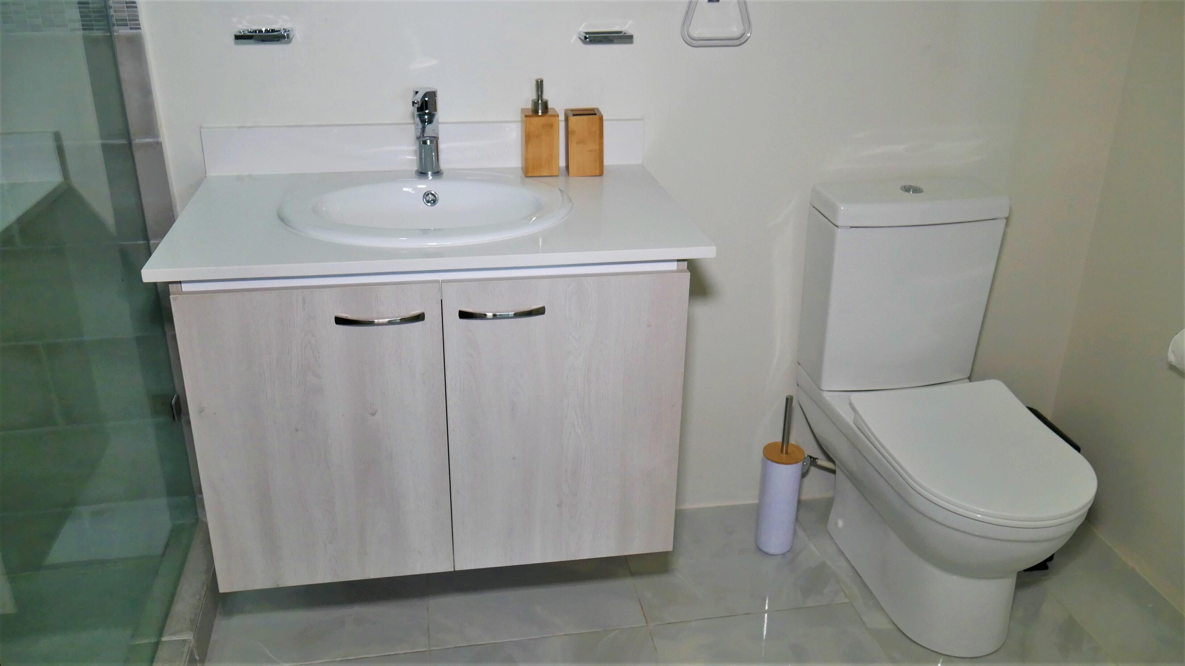 A bathroom with a white sink, wooden cabinets, a toilet, and a glass shower enclosure.