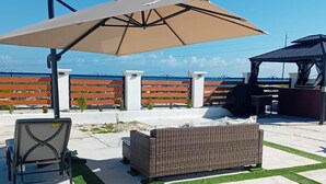 An outdoor patio area with a wicker sofa, a table, and an umbrella. - Lux Sea View Camelot Village Discovery Bay (Discovery Bay)