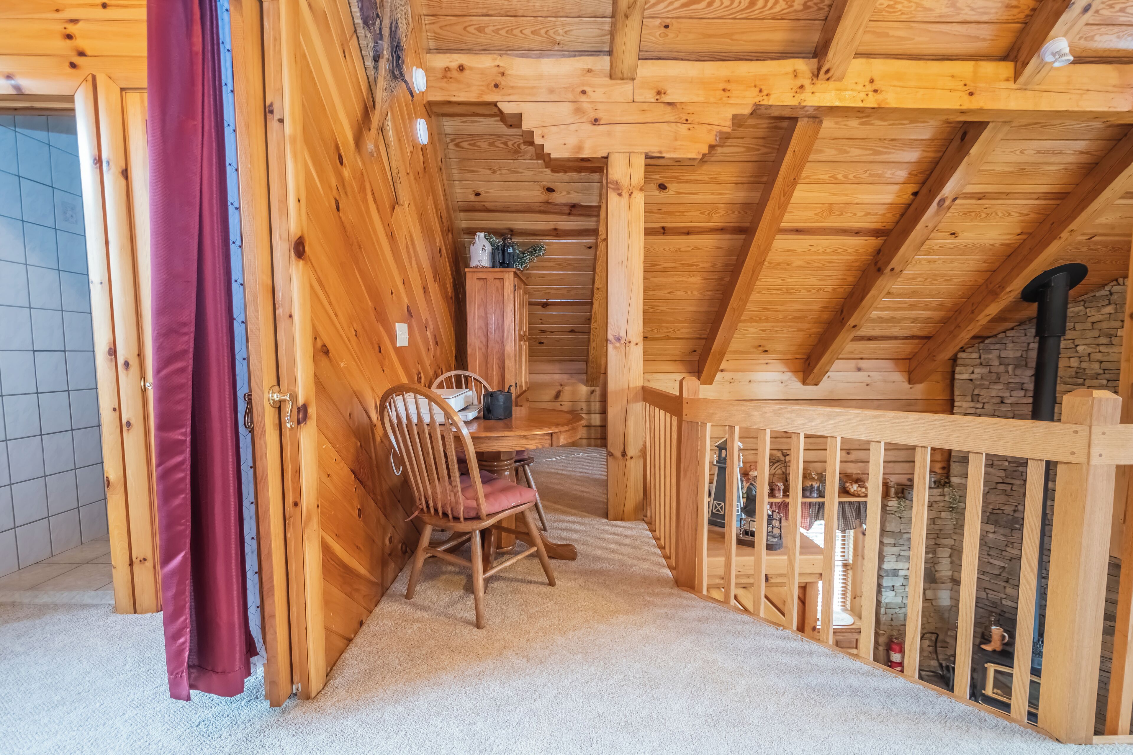 A wooden cabin interior with a dining area, a wooden chair, and a staircase leading to a lower level.