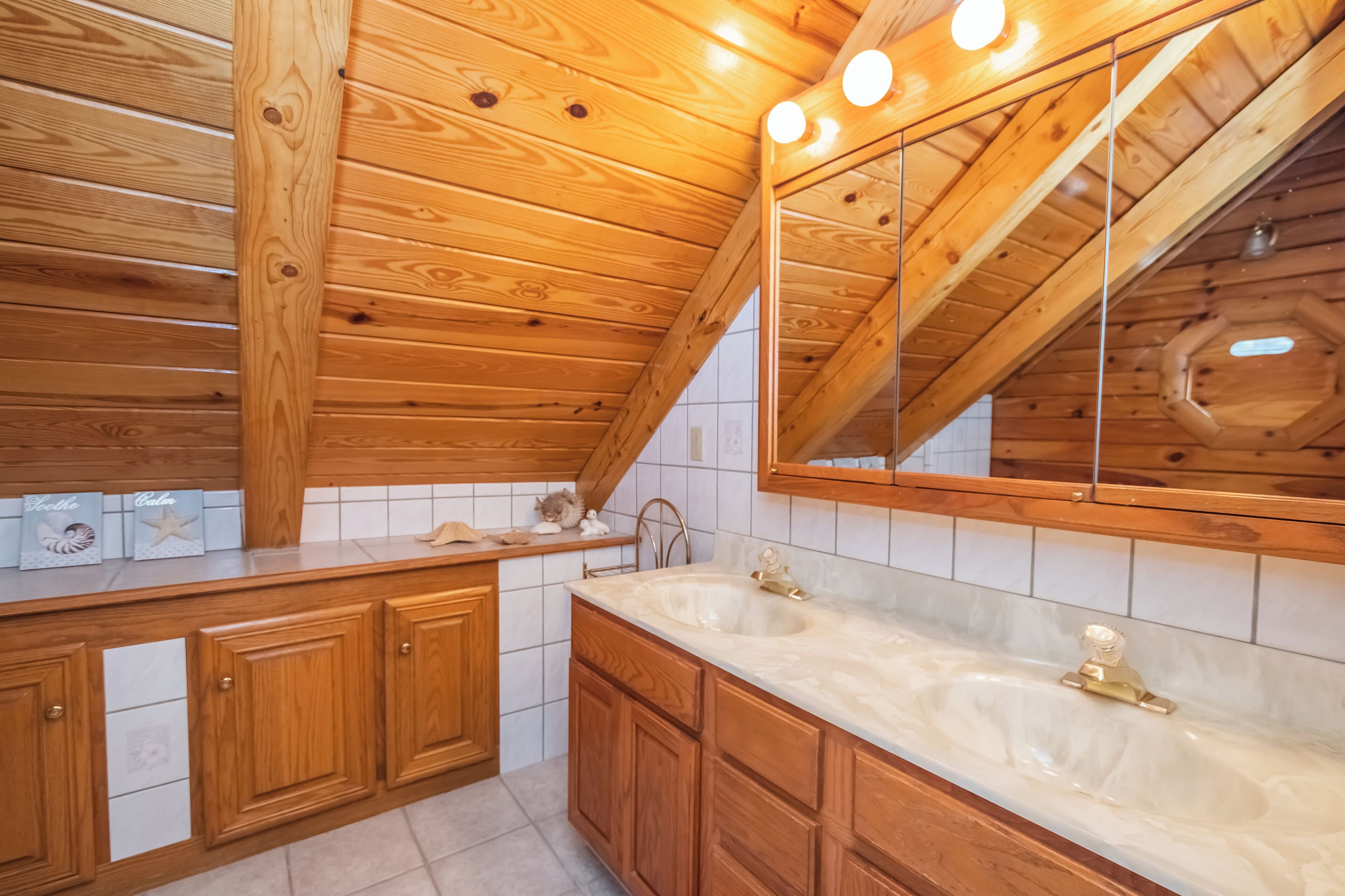 Un baño tipo cabaña de madera con un espejo grande, dos lavamanos y armarios de madera.