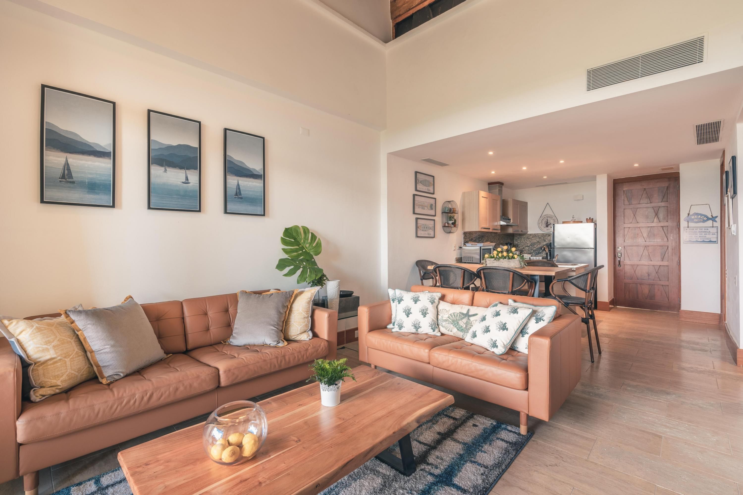 Una sala de estar moderna con un sofá de cuero marrón, una mesa de centro de madera y un comedor con una cocina al fondo.