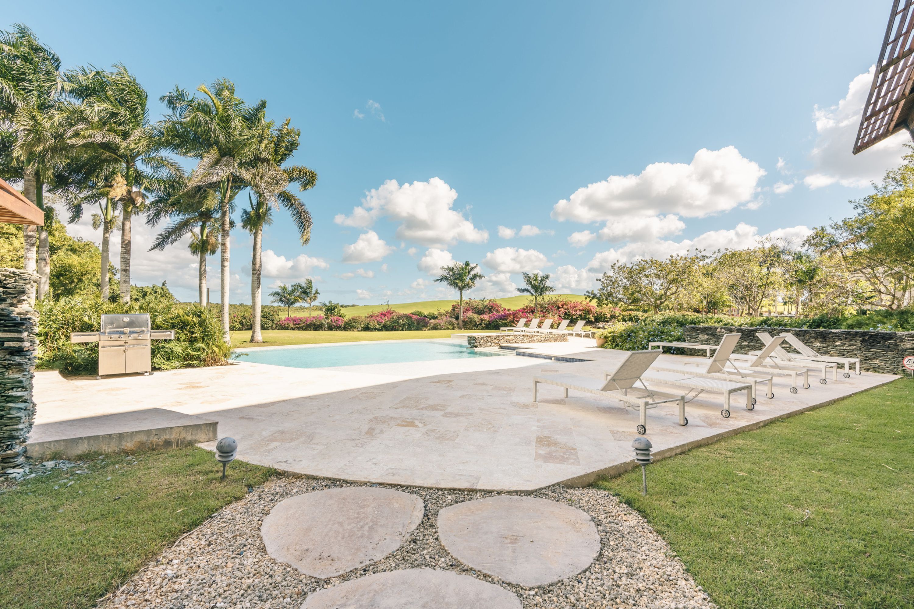 A pool area with lounge chairs, palm trees, and a barbecue grill.