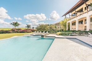A swimming pool with lounge chairs, a stone wall, and a building with a balcony. - 1BR 4 Guests Golf View Course Casa de Campo (La Romana)