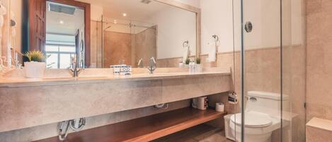 Un baño moderno con un espejo grande, cabina de ducha, inodoro y tocador con lavabo y encimera.