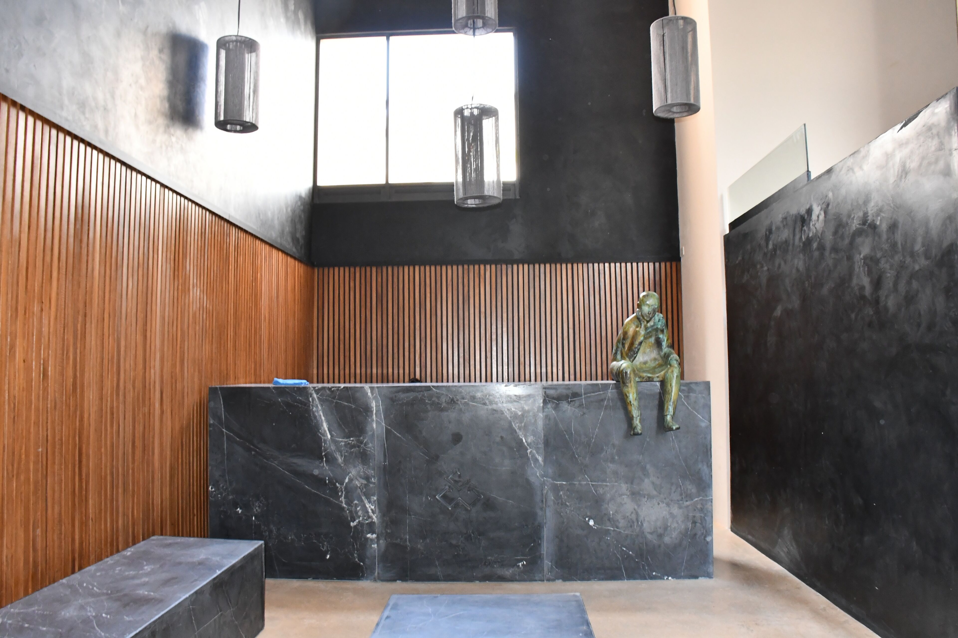 Un intérieur moderne avec un mur composé de lambris en bois, un banc en marbre noir et une statue en bronze.